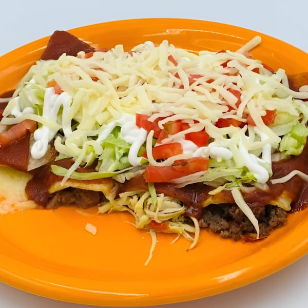 A plate of Carnales Taqueria enchiladas topped with red sauce, shredded lettuce, diced tomatoes, sour cream, and cheese.