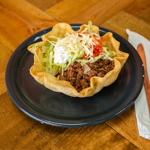 A taco salad in a crispy tortilla bowl, filled with ground beef, lettuce, cheese, tomatoes, and sour cream.