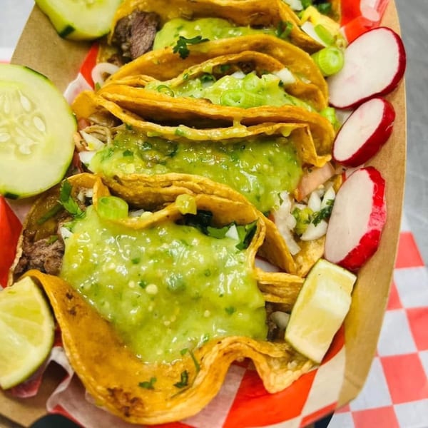 Close-up of Carnales Taqueria's tacos with green salsa, onions, cilantro, and lime, cucumbers, radishes.