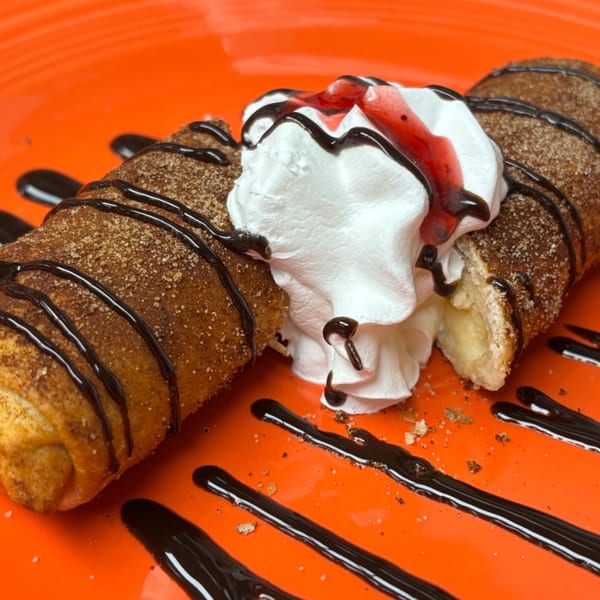 A Mexican dessert chimichanga, topped with whipped cream, chocolate, and strawberry syrup on an orange plate.