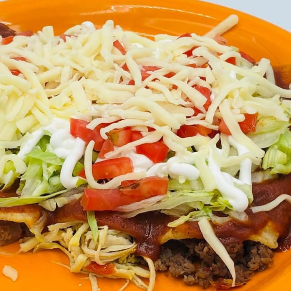 Close-up of a Mexican dish with shredded cheese, diced tomatoes, lettuce, and sour cream.