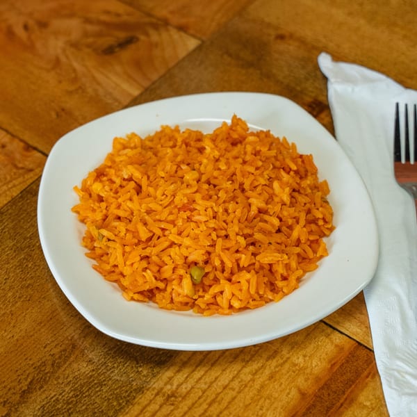 A white plate filled with vibrant orange Mexican rice, next to a white napkin and fork.