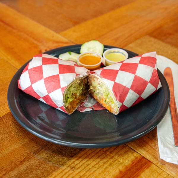 A Carnales Taqueria burrito, cut in half, wrapped in red and white checkered paper, with sauces.