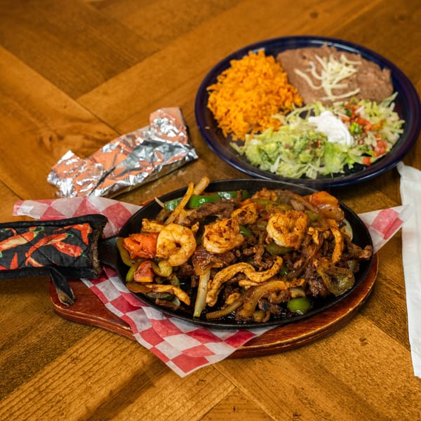Sizzling fajitas with shrimp, steak, chicken, and vegetables, served with rice, beans, and salad.