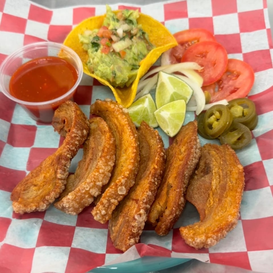 Crispy chicharrones, guacamole in a taco shell, salsa, sliced tomatoes, onions, limes, and jalapeños.