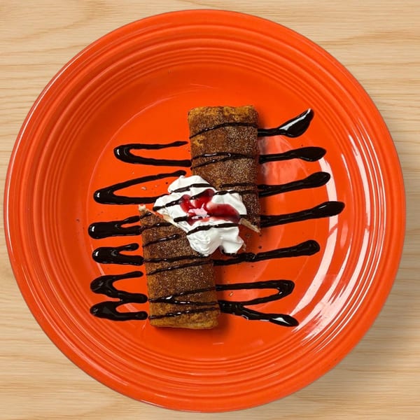 Two churros with whipped cream, strawberry sauce, and chocolate drizzle on an orange plate.