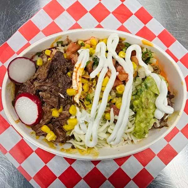 Overhead view of a Carnales Taqueria burrito bowl with meat, corn, radishes, guacamole, and sour cream.