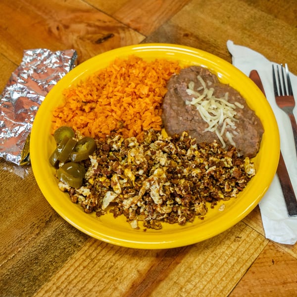 A yellow plate of Mexican food with rice, refried beans, scrambled eggs with chorizo, and jalapeños.