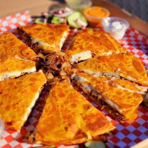 A large quesadilla cut into eight slices, filled with meat and cheese, served with caramelized onions.