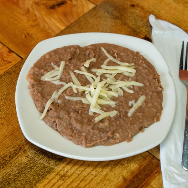 A white plate of refried beans topped with shredded cheese on a wooden table.