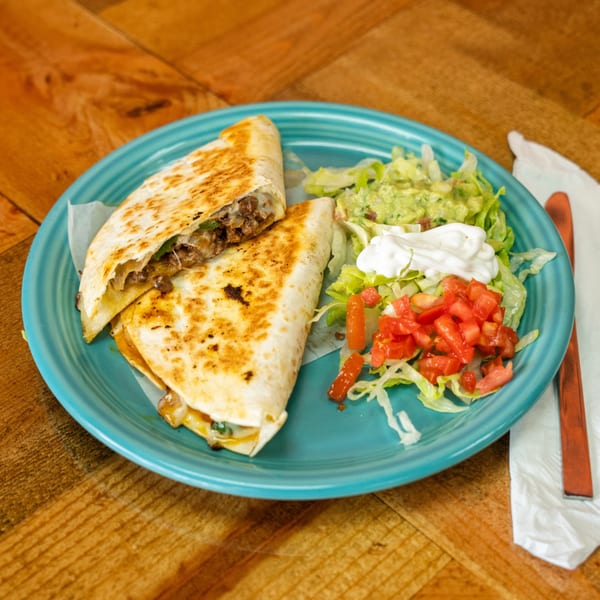 Two quesadilla halves with meat and cheese, served with guacamole, lettuce, sour cream, and diced tomatoes.