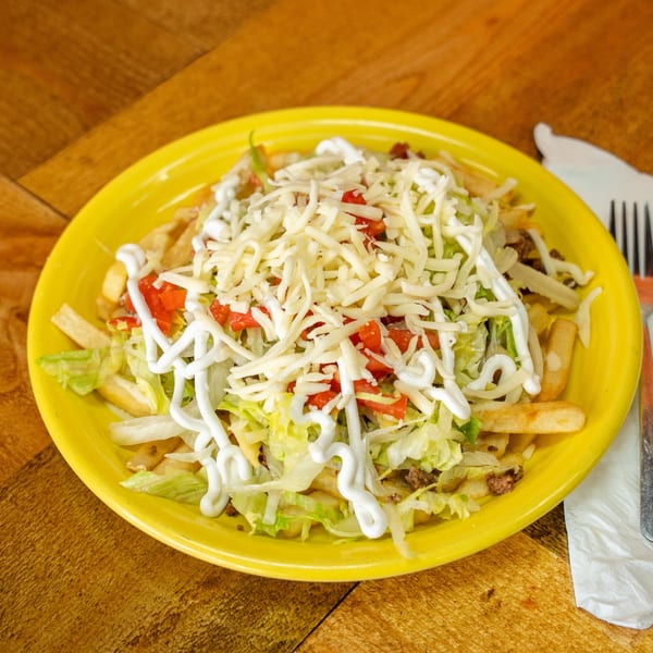 Carnales Taqueria's loaded fries with cheese, lettuce, tomatoes, and sour cream on a yellow plate.