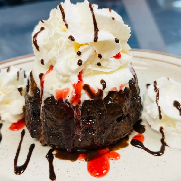 Chocolate lava cake topped with whipped cream, chocolate syrup, and strawberry drizzle on a plate.