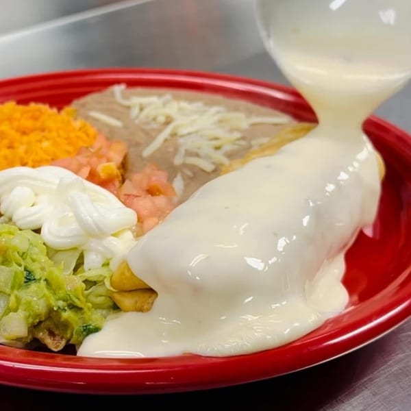 A burrito smothered in white cheese sauce, with sides of rice, beans, guacamole, and sour cream.