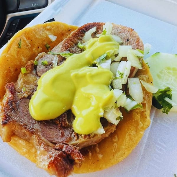 A close-up of a Carnales Taqueria taco with meat, onions, cilantro, and yellow sauce.