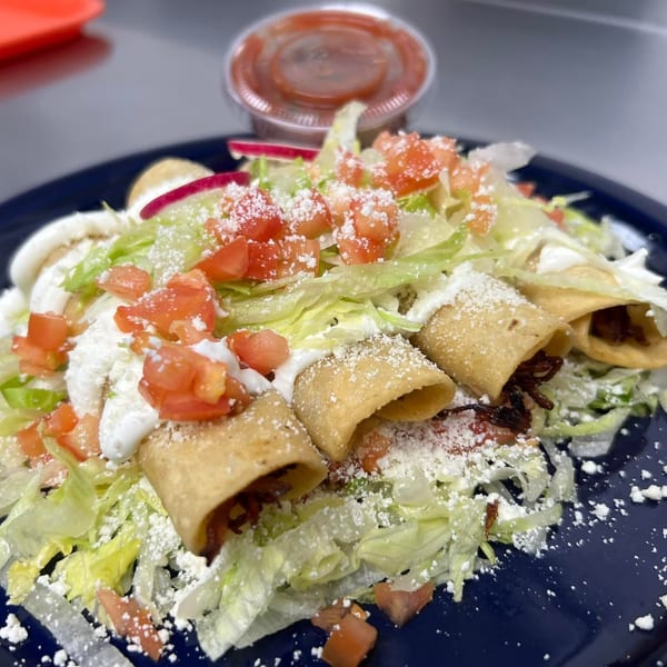 Crispy taquitos topped with shredded lettuce, diced tomatoes, sour cream, and cotija cheese, with salsa.