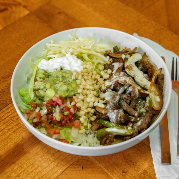 A Carnales Taqueria burrito bowl with steak, rice, guacamole, pico de gallo, corn, and sour cream.