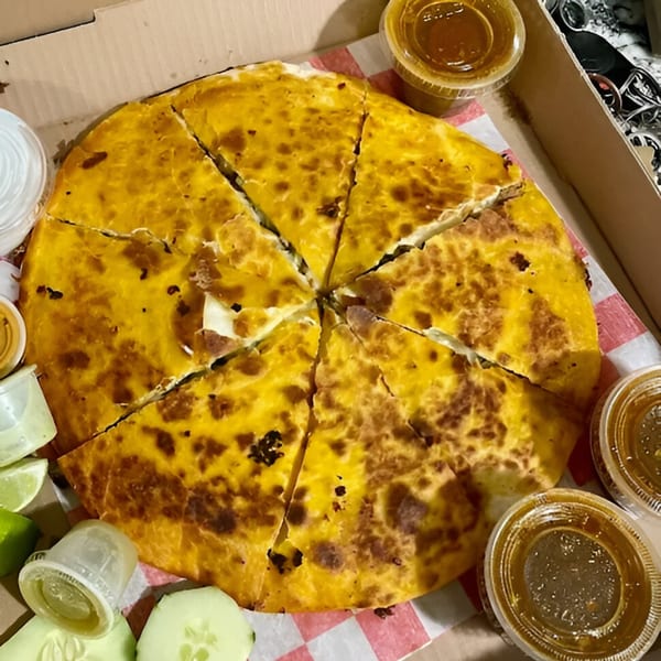 A large, round, golden-brown quesadilla, cut into wedges, with small sauce cups and lime slices.