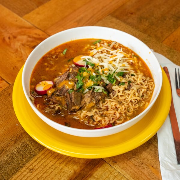 A bowl of Carnales Taqueria's birria ramen with beef, noodles, cheese, cilantro, and radishes.